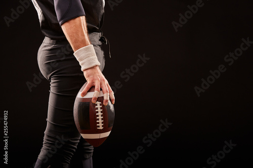 Mid section of American football player with ball against black, copy space, side view