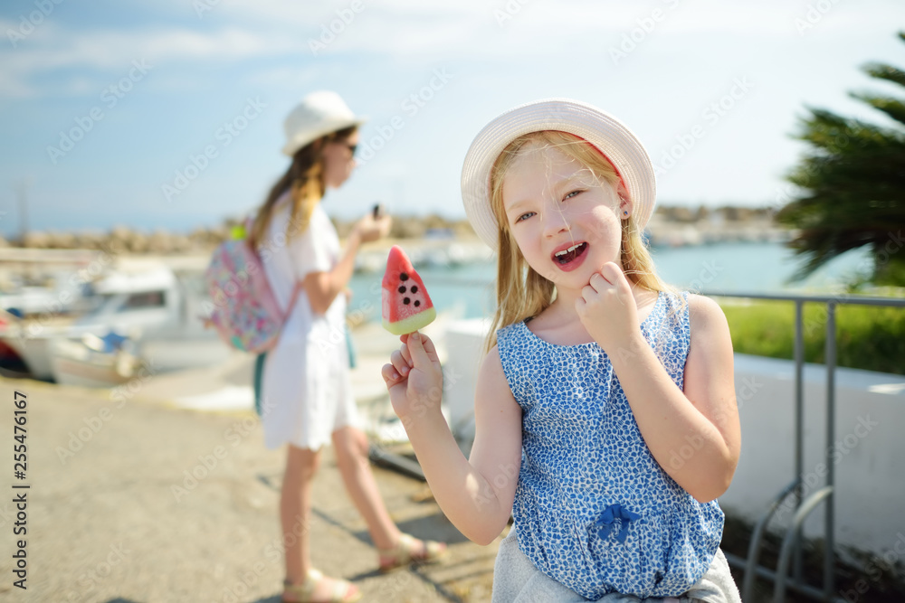 Two cute young sisters having an ice-cream on warm and sunny summer day during family vacations in Greece