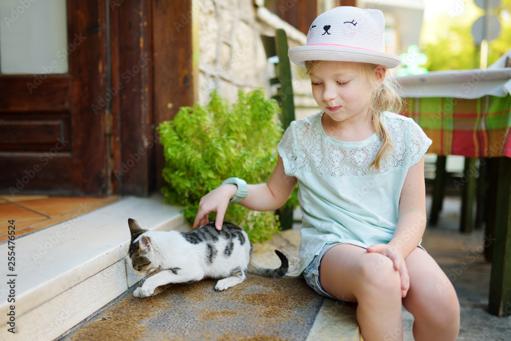 Cute young girl petting a friendly Greek cat on warm and sunny summer day during family vacations in Kalavryta, Greece Cute young girl petting a friendly Greek cat on warm and sunny summer day during family vacations in Kalavryta, Greece