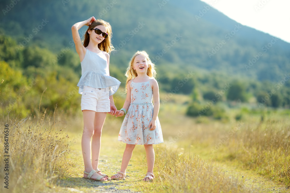 Fototapeta premium Two cute young sisters laughing and hugging on warm and sunny summer day during family vacations in Greece