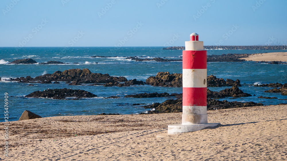 Vibrant red and white lighthouse at beach on sunny day in Portugal