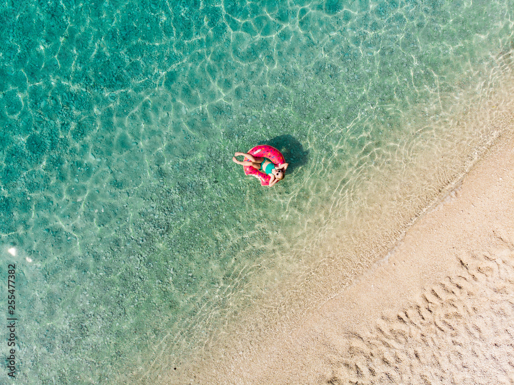 Naklejka premium Aerial top down view of cute young girl floating on toy ring at Myrtos beach, the most beautiful beach of Kefalonia, a large coast with turqoise water and white coarse sand.
