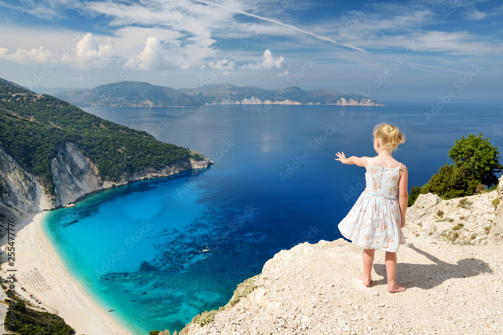 Little girl enjoying the view of picturesque jagged coastline of Kefalonia with clear turquoise waters, surrounded by steep cliffs. Little girl enjoying the view of picturesque jagged coastline of Kefalonia with clear turquoise waters, surrounded by steep cliffs.