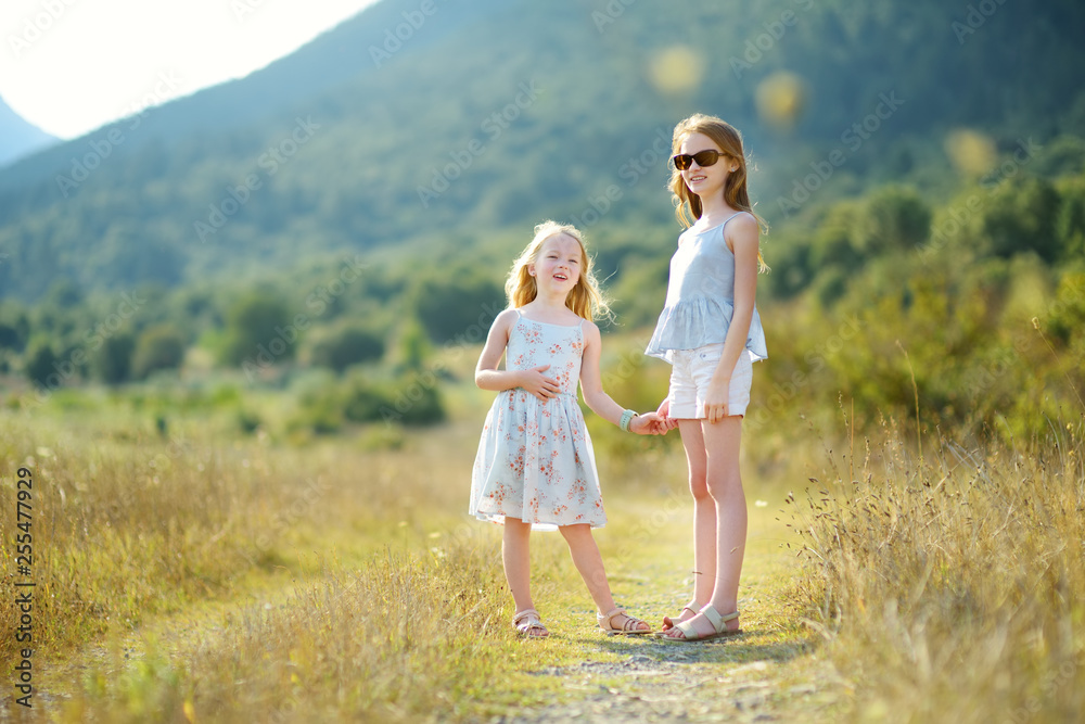 Two cute young sisters laughing and hugging on warm and sunny summer day during family vacations in Greece