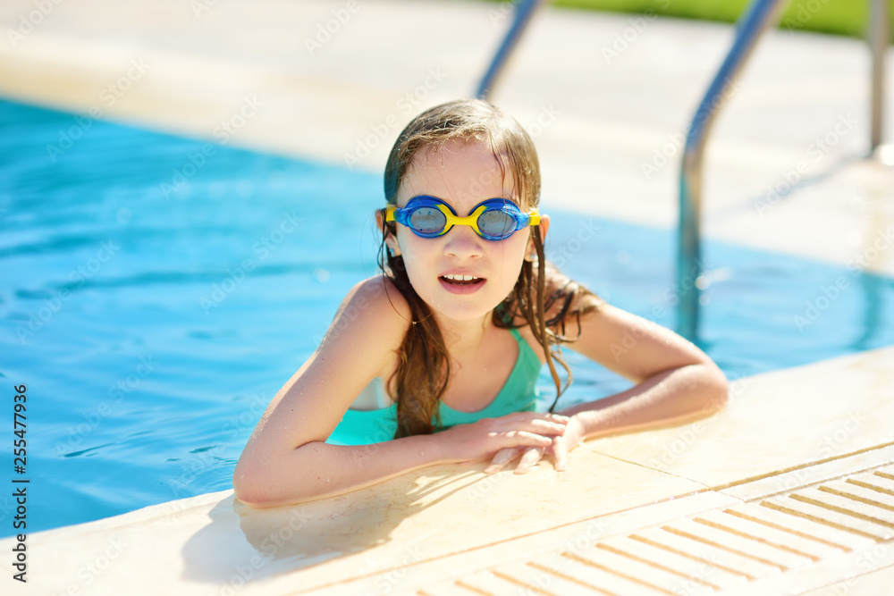 Cute young girl wearing swimming goggles having fun in outdoor pool. Child learning to swim. Kid having fun with water toys.