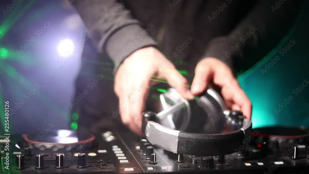 DJ Spinning, Mixing, and Scratching in a Night Club, Hands of dj tweak various track controls on dj's deck, strobe lights and fog, or Dj mixes the track in the nightclub at party. Selective focus