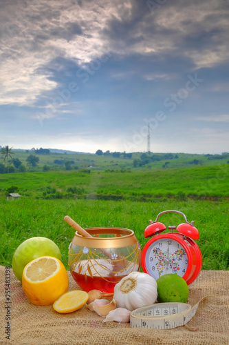 Measuring tape, red alarm clock , garlic, green apple,lime  , lime , lemon , dipper  and honey  on jute with beautiful blurred background   . Healthy eating photo