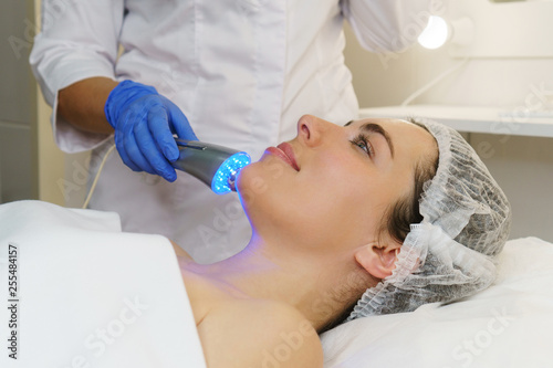 Hardware cosmetology. Ultrasound chromotherapy. Beautician carries out procedure for tightening skin of face. Spa.