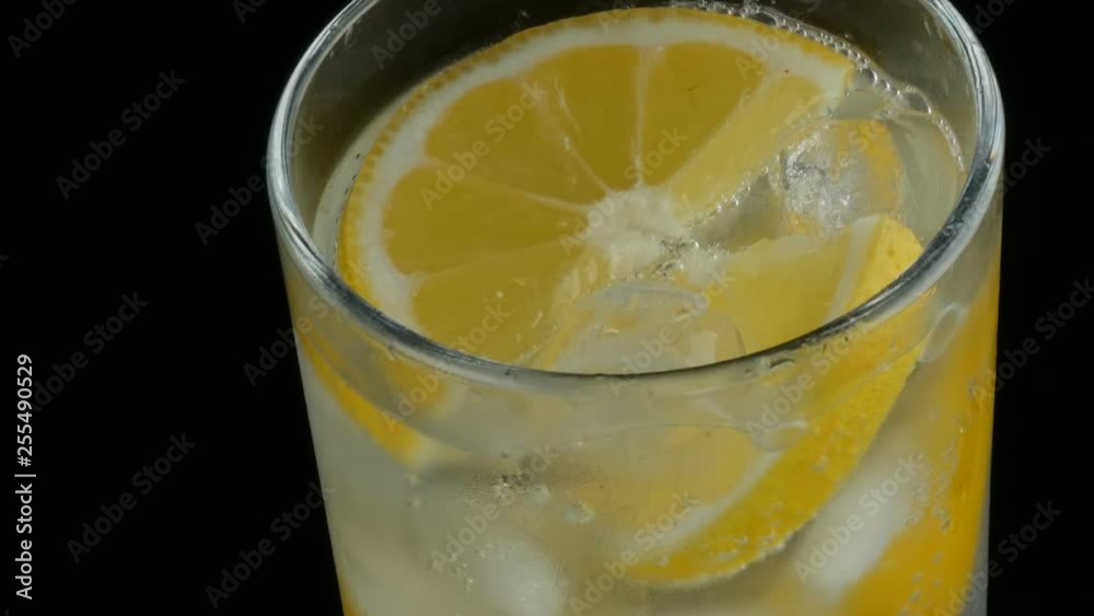 Sliced lemon in a long glass with ice cubes and cold soda on a black background close up view. Refreshing Lemonade Bubbles Sliced lemon in a long glass with ice cubes and cold soda on a black background close up view. Refreshing Lemonade Bubbles