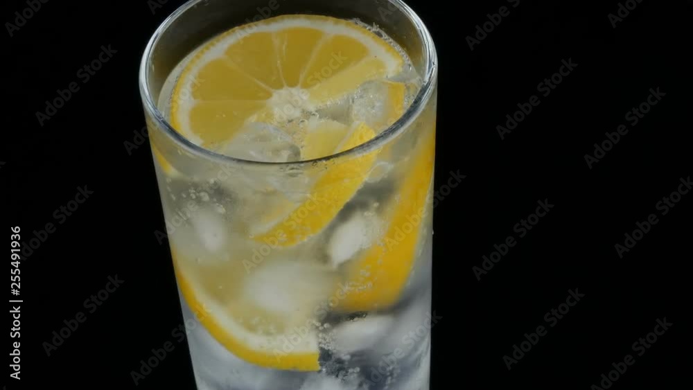 Sliced lemon in a long glass with ice cubes and cold soda on a black background close up view. Refreshing Lemonade Bubbles