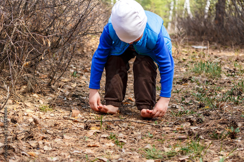 a four-year-old child walks barefoot on dry grass and leaves in the forest