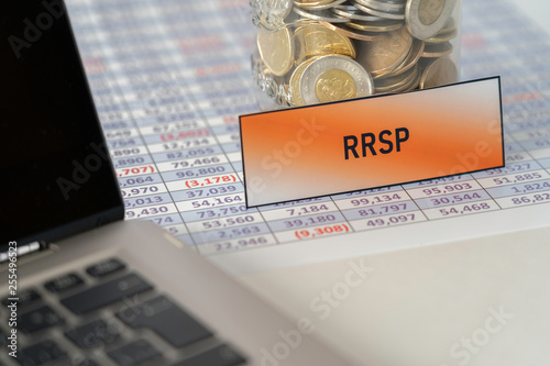 Jar full of Coins for RRSP on spreadsheet next to Laptop photo