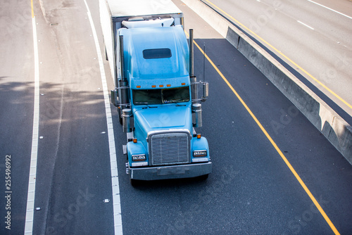 Classic blue big rig bonnet semi truck transporting cargo in refrigerator semi trailer moving on wide road