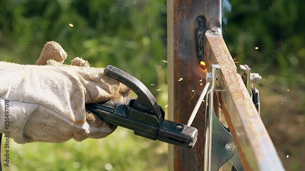 close view skilled worker in protective gloves connects plank to fence with welding tool in yard close view skilled worker in protective gloves connects plank to fence with welding tool in yard