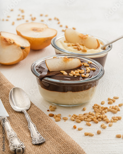 Chocolate and vanilla pudding with pine nuts, and Asian pear slices in a glass bowls on white background. Healthy, tasty, gluten free breakfast