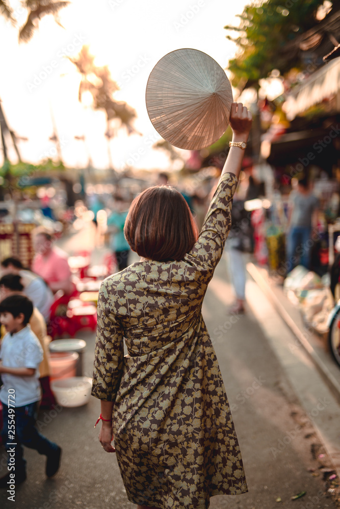 Obraz premium Tourist woman is wearing Non La (Vietnamese tradition hat) and enjoy sightseeing at Heritage village in Hoi An city in Vietnam.