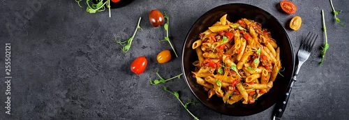 Panel kuchenny z motywem Penne pasta in tomato sauce with meat, tomatoes decorated with pea sprouts on a dark table. Top view. Banner