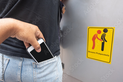 Thief stealing mobile phone from back pocket of a woman with beware pickpockets sign symbol background