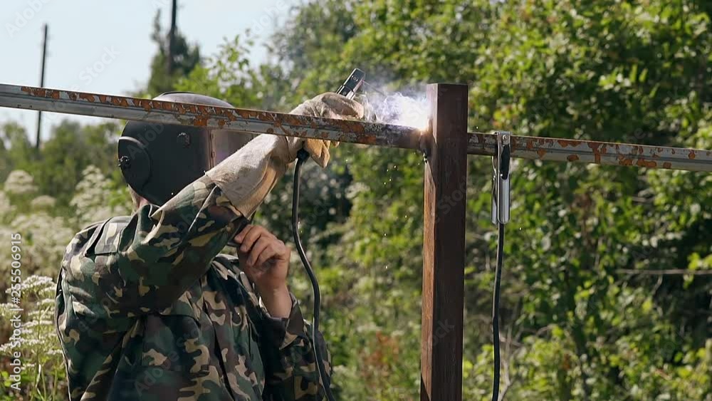 slow motion skilled craftsman in protective mask welds metal rail of new fence with modern tool on day slow motion skilled craftsman in protective mask welds metal rail of new fence with modern tool on day