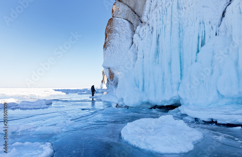 Lake Baikal in March. Beautiful icy cliffs of Olkhon Island. Lonely photographer seems small compared to the huge icicles on the rocks