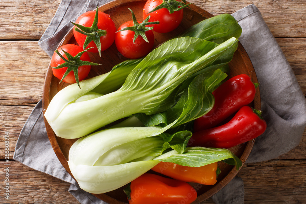 Vegetable assorted fresh baby bok choy, tomatoes and peppers close-up on a plate on a wooden table. Horizontal top view Vegetable assorted fresh baby bok choy, tomatoes and peppers close-up on a plate on a wooden table. Horizontal top view