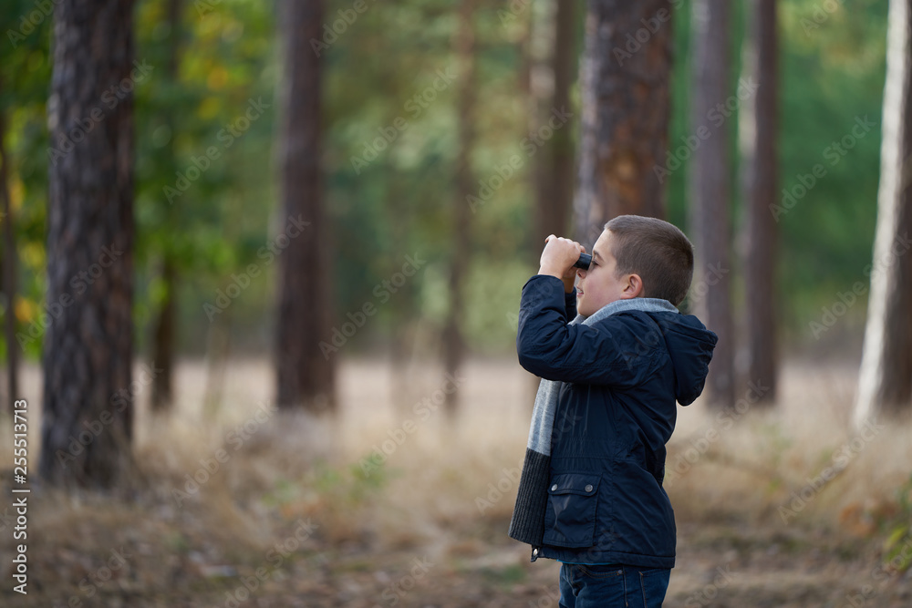 A boy with blue jacket looking through binoculars in the forest A boy with blue jacket looking through binoculars in the forest