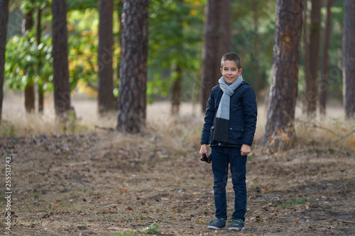 A smiling boy with blue jacket holding  binoculars in the forest 