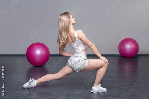 Blond Sporty Caucasian Lady is in the Gym during Training, Exercises to stretch the muscles on the legs. Warm-up before training. Women's fitness. photo