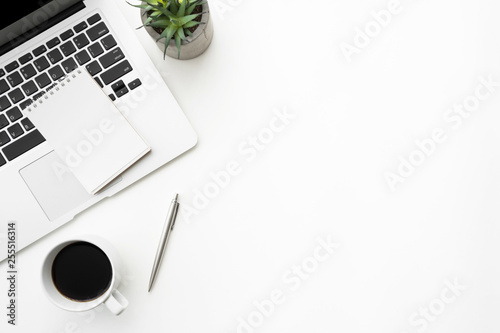 White office desk table with notebook over a laptop computer with coffee and supplies. Top view with copy space, flat lay.