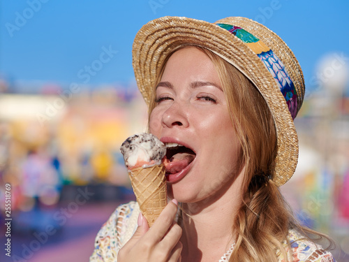 Young beautiful girl in sunhat is eating tasty ice-cream in the Luna park.
