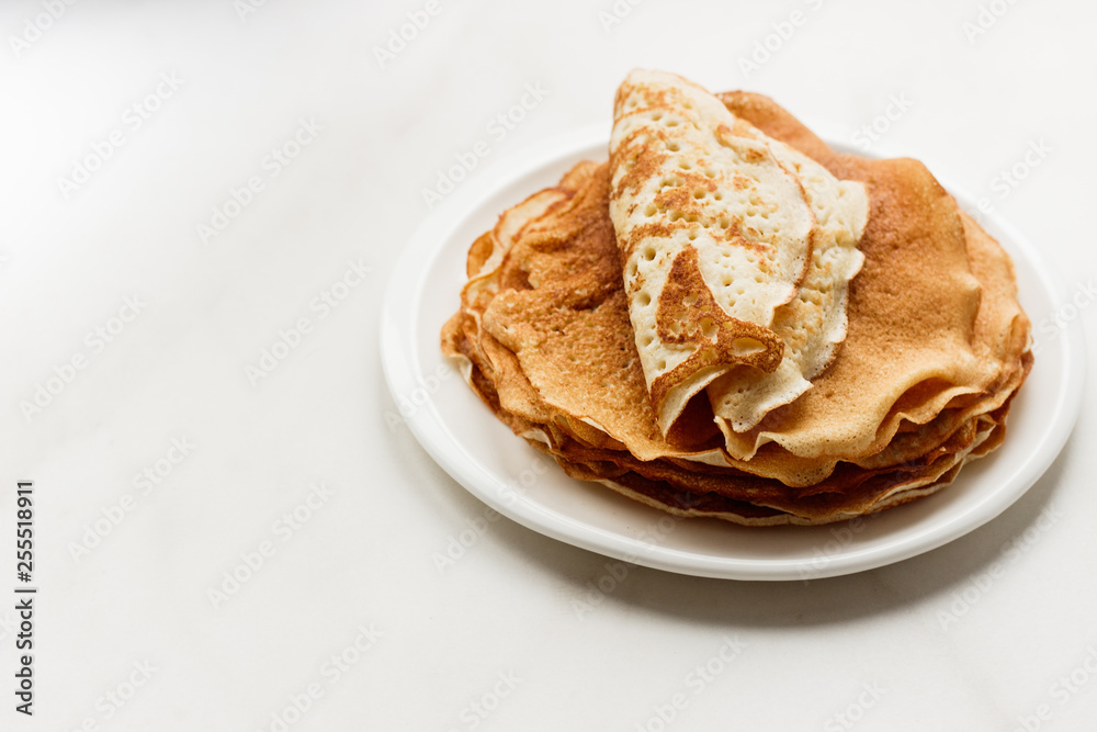 Staple of wheat golden yeast pancakes or crepes in a white plate closeup on a white background