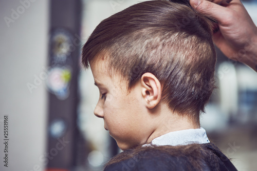 The portrait of a cute European boy in a barbershop. He is getting his new hairstyle...