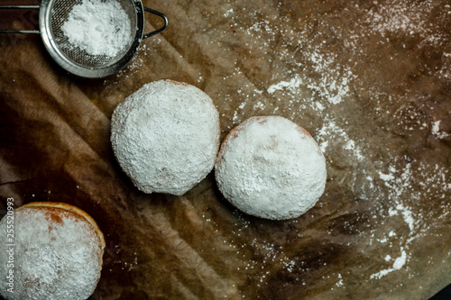 fresh, homemade fluffy donuts with powdered sugar on baking paper, on the kitchen table