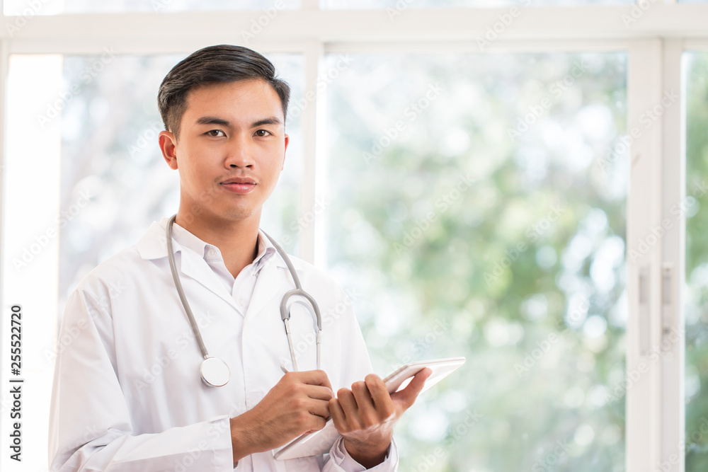 Smart male Doctor using tablet computer looking camera with white gown suite wearing Stethoscope on neck for seaching information treating patients in hospital or clinic, Healthcare medical concept Smart male Doctor using tablet computer looking camera with white gown suite wearing Stethoscope on neck for seaching information treating patients in hospital or clinic, Healthcare medical concept