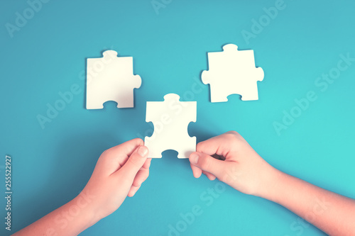 Jigsaw puzzle piece in a hand. Teamwork and solution or idea concept with copy space on trendy blue background