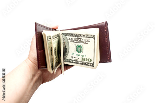Female hand holds opened brown wallet with a thick wad of bills. isolated over a white background.