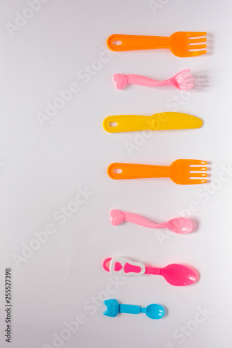 Children plastic dishes on a white background, forks, spoons, plate with space for text. Flat lay, top view minimal concept.