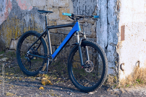 A modern blue mountain bike stands at a vintage brick wall with old concrete.