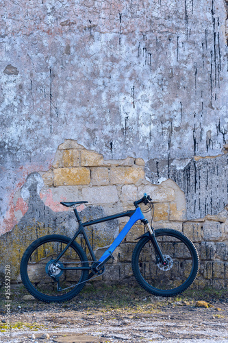 A modern blue mountain bike stands at a vintage brick wall with old concrete.