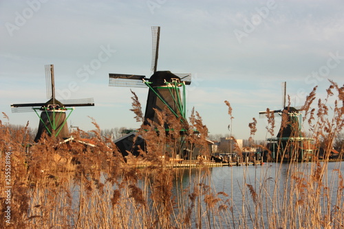 symbol of a tradition now lost, now a mere tourist attraction. colorful windmills built of wood still overlook the water of the river of zaanse schans on which it reflects their vintage image photo