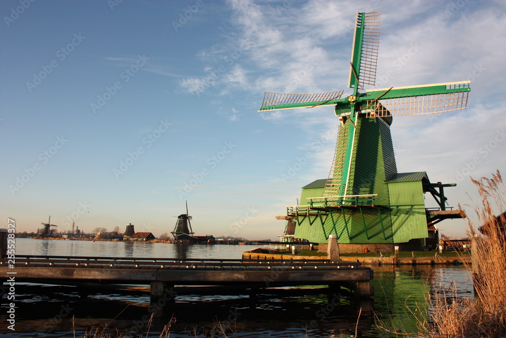symbol of a tradition now lost, now a mere tourist attraction. colorful windmills built of wood still overlook the water of the river of zaanse schans on which it reflects their vintage image