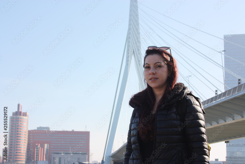 European tourist girl on a trip to the Netherlands. the person smiles posing under the Erasmus Bridge in Rotterdam, the Netherlands, amid a little haze