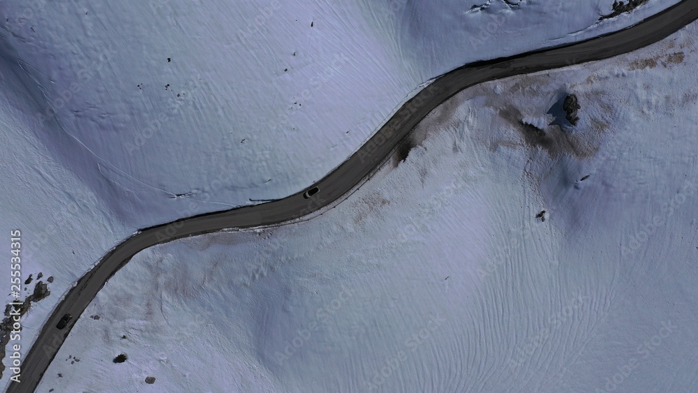 Aerial drone top view photo of snowed mountain curved - snake asphalt road crossing in beautiful winter scene