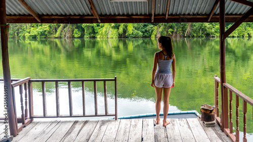 Young Asian girl standing on covered deck by a peaceful river