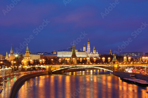 Illuminated Moscow Kremlin and Bolshoy Kamenny Bridge in the rays of setting sun. View from the Patriarshy pedestrian Bridge in Russia. Evening urban landscape in the blue hour