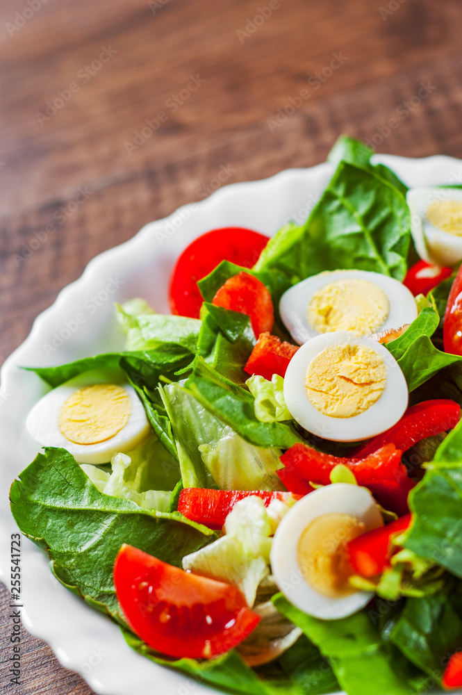 spinach salad with eggs, pepper and tomatoes in white plate on wooden table background spinach salad with eggs, pepper and tomatoes in white plate on wooden table background