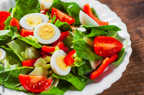 spinach salad with eggs, pepper and tomatoes in white plate on wooden table background