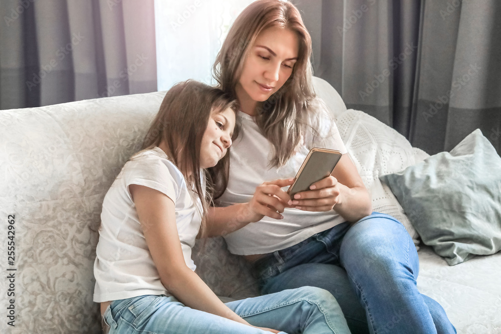 mom and daughter are sitting on the couch at home with the phone mom and daughter are sitting on the couch at home with the phone