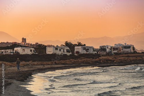 Motorhome making wild camp on the beach at a beautiful sunset or sunrise with mountains in the background. Caravan parked on the beach in front of the blue sea in a beautiful place of wild nature