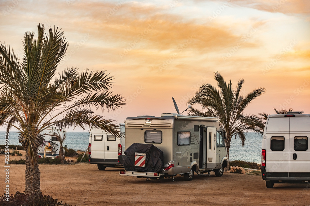 Motorhome making wild camp on the beach at a beautiful sunset or sunrise with mountains in the background. Caravan parked on the beach in front of the blue sea in a beautiful place of wild nature - obrazy, fototapety, plakaty 